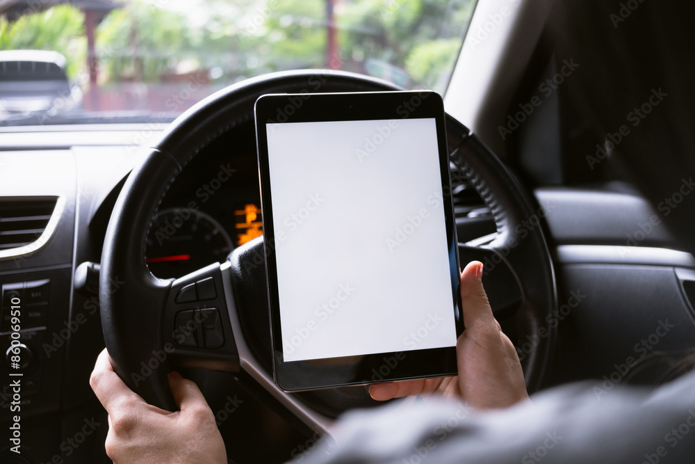 Woman sitting in a car and holding a tablet with blank screen.