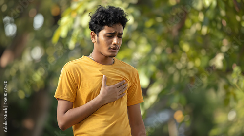 The tired young male Indian athlete stood bent over in the park with his hand over his chest, suffering severe pain and shortness of breath after jogging