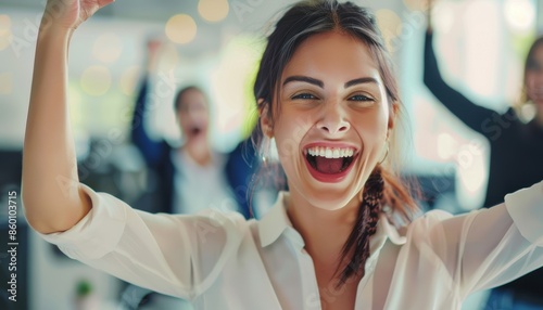 A joyful woman celebrating success at the office with colleagues cheering in the background, showing teamwork and achievement.