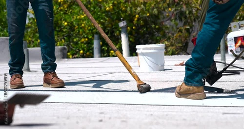 Roofer applying granulated APP Torch Down and Using a Roller