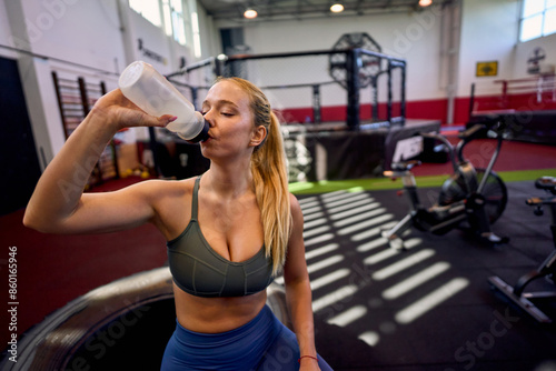 Athletic female taking a drink of water during a recovery break at the gym, staying hydrated between intense workouts. © DusanJelicic