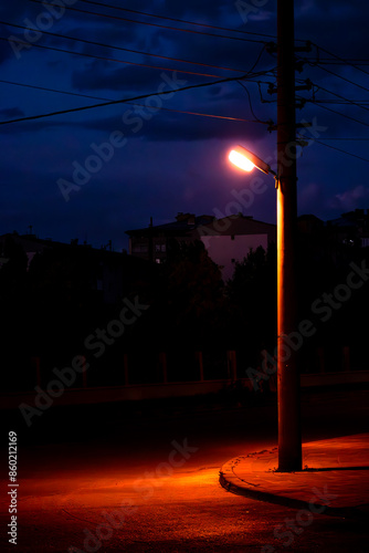 A dramatic streetlight casting an orange glow on the empty street, evoking feelings of isolation and tranquility.
