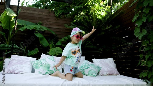 Funny cute girl drinks a cocktail on summer vacation. The child has fun on the beach. Cute baby in a colorful swimsuit and sunglasses is resting.