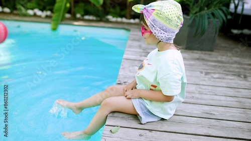 Funny cute girl drinks a cocktail on summer vacation. The child has fun on the beach. Cute baby in a colorful swimsuit and sunglasses is resting.