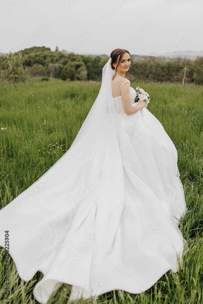 A bride is walking through a field wearing a white dress. She is holding a bouquet of flowers A bride is walking through a field wearing a white dress. She is holding a bouquet of flowers