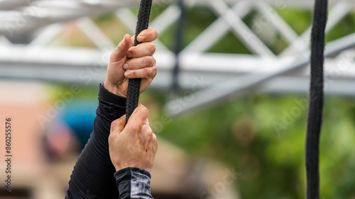 Hands grasp a rope at a hanging obstacle in an obstacle course
