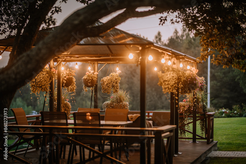 Blome, Latvia - September 11, 2023 - A cozy outdoor gazebo with hanging plants and string lights at dusk, surrounded by greenery, creating a warm and inviting atmosphere photo