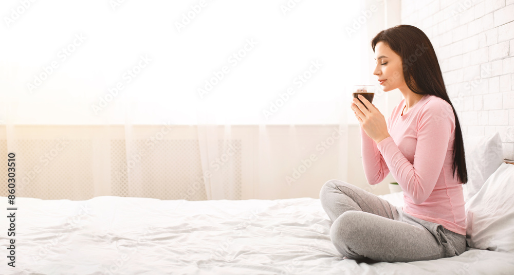 Satisfying aroma. Pleased girl enjoying fresh hot coffee in morning, sitting in bed, free space Satisfying aroma. Pleased girl enjoying fresh hot coffee in morning, sitting in bed, free space