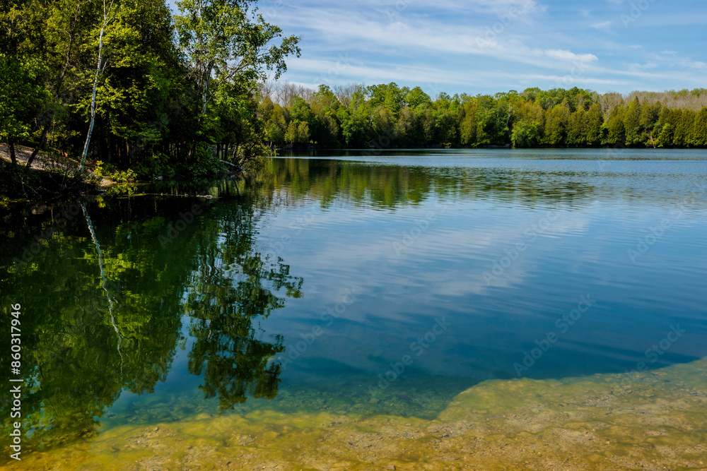 A calm lake water of Quarry Lake in early June unter the slightly streaking clouds and blue sky at Harrington Beach State Park, Belgium, Wisconsin A calm lake water of Quarry Lake in early June unter the slightly streaking clouds and blue sky at Harrington Beach State Park, Belgium, Wisconsin