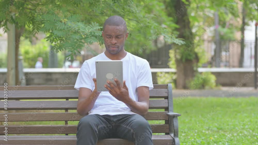 African American Man Using Tablet while Sitting on Bench in Park African American Man Using Tablet while Sitting on Bench in Park