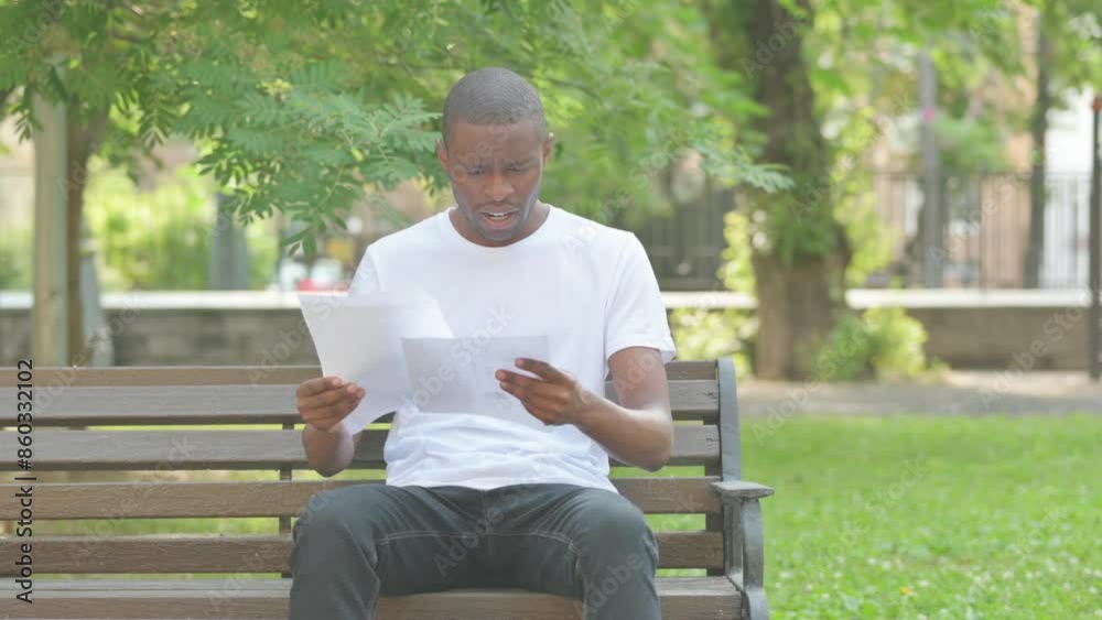 African American Man Upset by New Contract while Sitting on Bench in Park African American Man Upset by New Contract while Sitting on Bench in Park