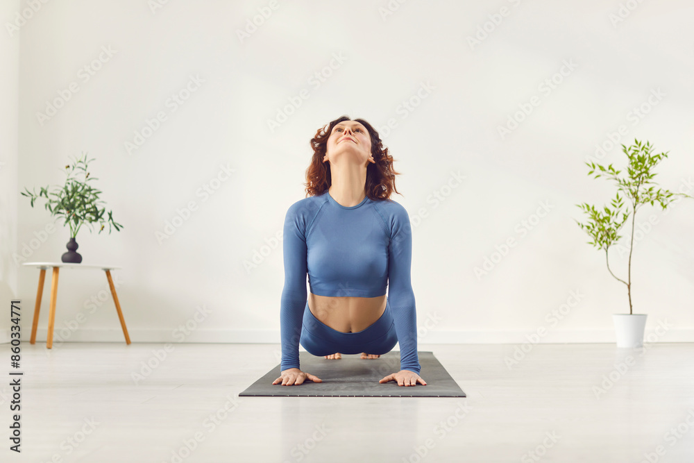 Fototapeta premium Yogi sporty woman practicing yoga, doing upward facing dog exercise, Urdhva mukha shvanasana pose, working out, wearing sportswear, indoor full in white yoga studio, home among green homeplants 