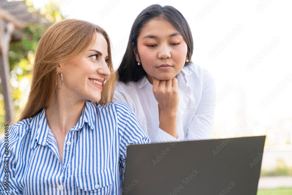 Happy young multiethnic couple spending time together at the park, studying while sitting at the table with laptop Happy young multiethnic couple spending time together at the park, studying while sitting at the table with laptop