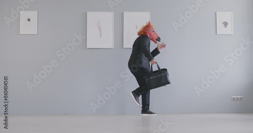Eccentric young man in black business suit and funny animal masquerade brown horse mask jumping up, dancing with business bag in his hand and celebrating the successful deal. 4k video photo