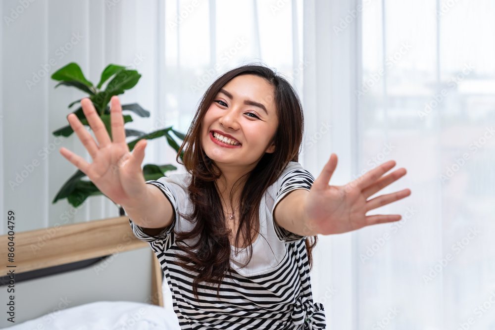 Joyful young Asian woman reaching out and smiling indoors, video call, looking at camera Joyful young Asian woman reaching out and smiling indoors, video call, looking at camera