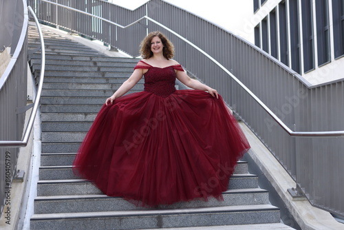 Frau im pompösen roten Abendkleid geht eine Treppe runter, lächelnd photo