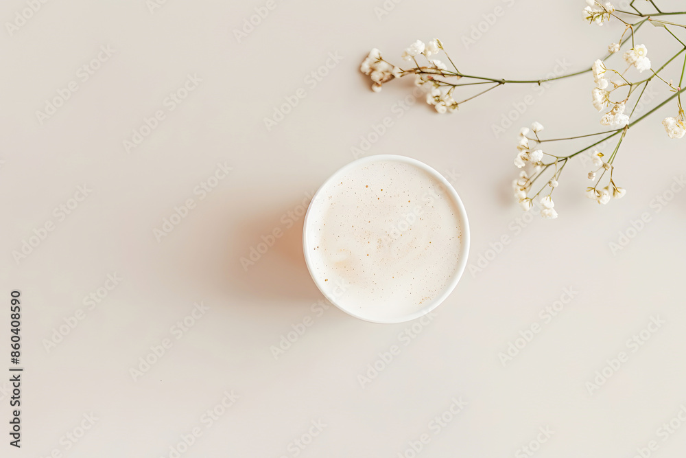 Minimalist overhead view of a frothy coffee in a white cup next to delicate white flowers on a light beige background. Minimalist overhead view of a frothy coffee in a white cup next to delicate white flowers on a light beige background.