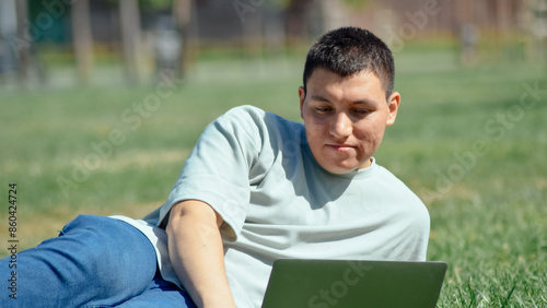 Young man in front of the computer notebook laptop lying on the grass in the park © Tark