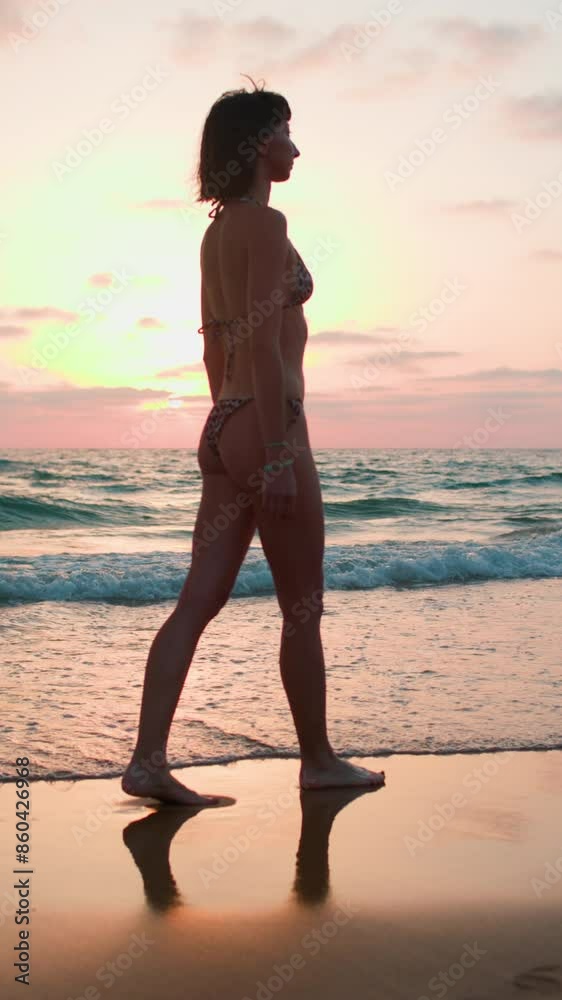 vertical shot. enjoying a walk on the beach. Slender woman in a swimsuit walks along the beach at sunset. A girl walks barefoot on the beach at sunset. vertical shot. enjoying a walk on the beach. Slender woman in a swimsuit walks along the beach at sunset. A girl walks barefoot on the beach at sunset.