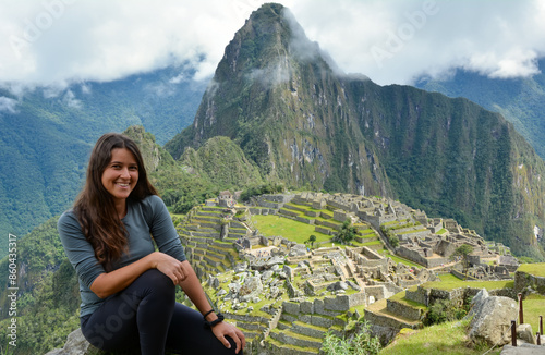 Attractive young Latina brunette woman with long hair sitting in the ruins of Machu Picchu and happy after arriving at one of the seven wonders of the world wearing sports clothes photo