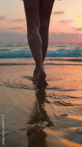 vertical shot. enjoying a walk on the beach. legs close up.  Slender woman in a swimsuit walks along the beach at sunset. A girl walks barefoot on the beach at sunset.