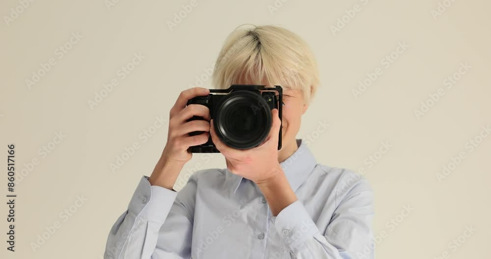 Cheerful woman with dyed blonde hair smiles taking pictures with professional camera. Young photographer does photoshoot in studio slow motion