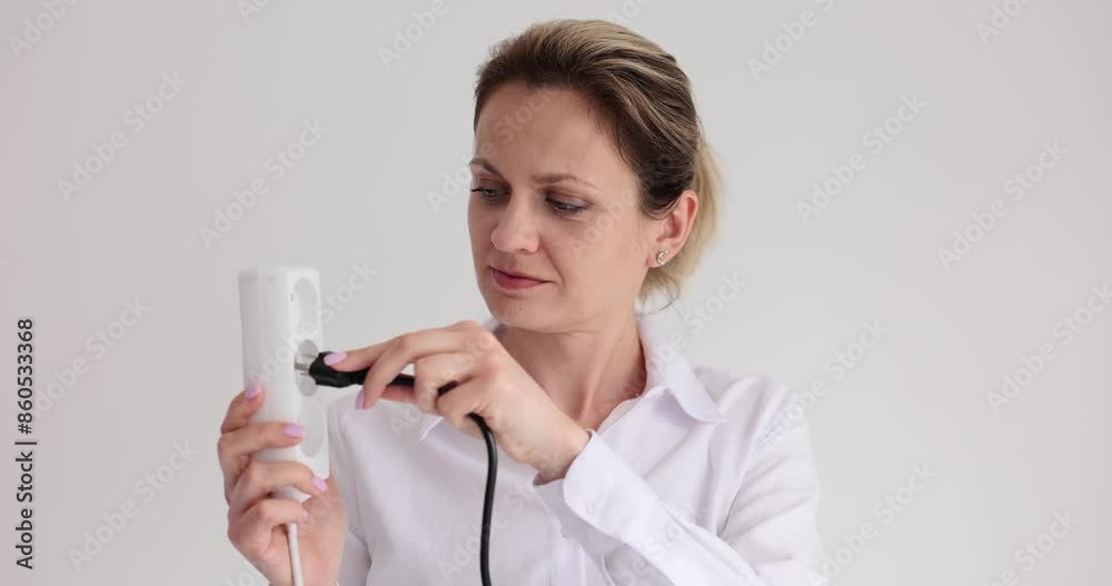 Woman confused by wrong plug and socket near white wall in office. Lady in blouse can not connect appliance to electrical network in studio Woman confused by wrong plug and socket near white wall in office. Lady in blouse can not connect appliance to electrical network in studio