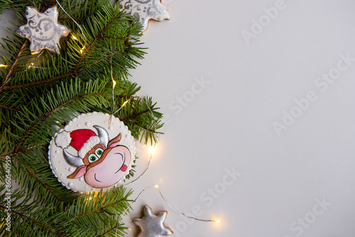 Close-up of Christmas tree branches decorated with festive ornaments, including gingerbread symbol ox of Chinese new year in Santa hat, candy canes, star cookies, illuminated by warm fairy lights.
