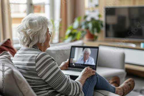 Elderly woman is sitting on her couch, having a video call with a doctor on her laptop