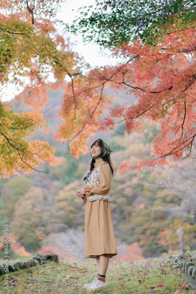 Asian woman in Japan's fall beauty, a cheerful holiday portrait amid yellow and red foliage. A journey capturing the essence of nature, fashion, and casual elegance.