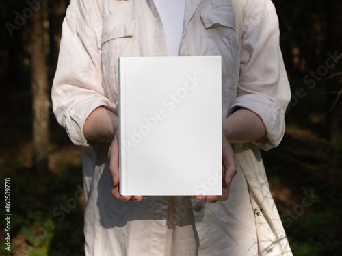 . Blank book hardback mockup in hand in nature, sunny day.