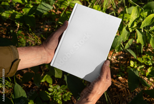 Foto . Male hands holding book hard cover mockup, blank hardcover mock up in nature,