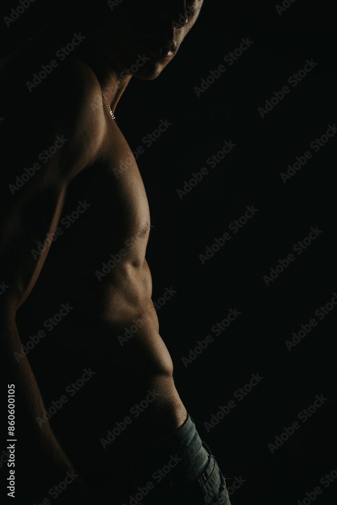 Artistic low light portrait of a shirtless man highlighting his muscular physique and toned abs against a dark background. Artistic low light portrait of a shirtless man highlighting his muscular physique and toned abs against a dark background.