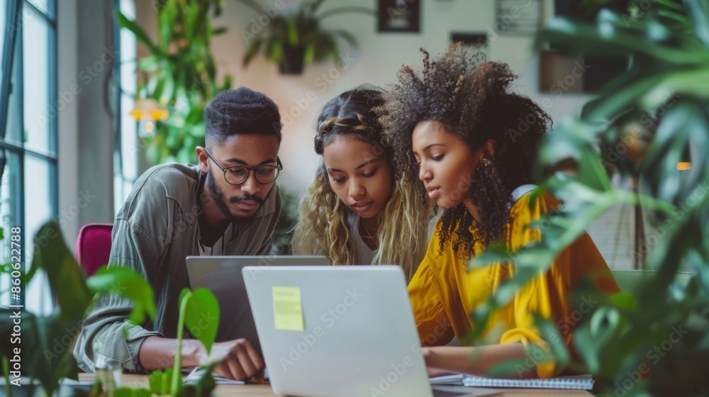 Three colleagues from diverse backgrounds are working together in a workspace filled with greenery, collaborating on a laptop and surrounded by modern design elements and open spaces. Three colleagues from diverse backgrounds are working together in a workspace filled with greenery, collaborating on a laptop and surrounded by modern design elements and open spaces.
