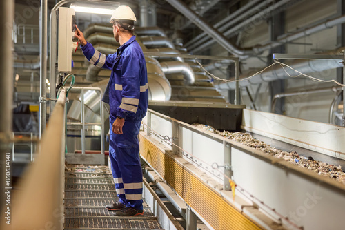 Фотография A technician wearing blue overalls and a white helmet operates machinery at an i