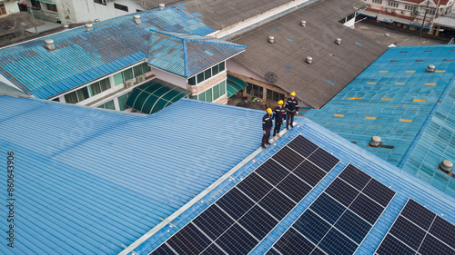 Aerial view of engineer worker standing on rooftop checking on solar cell panels installed on roof of the factory with professional team. Electric power industry renewable energy.