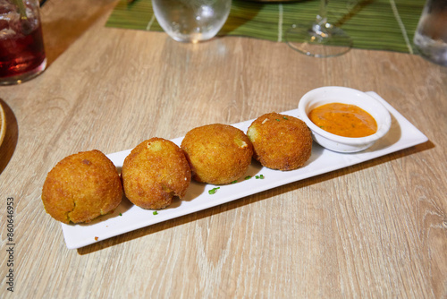 Fototapeta Naklejka Na Ścianę i Meble -  Sicilian arancini balls or risotto croquettes with tomato sauce on a white tray on a restaurant table