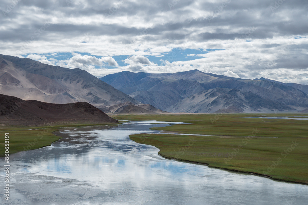 A river flows through a grassy field with distant mountains, Ladakh, Himalayas A river flows through a grassy field with distant mountains, Ladakh, Himalayas