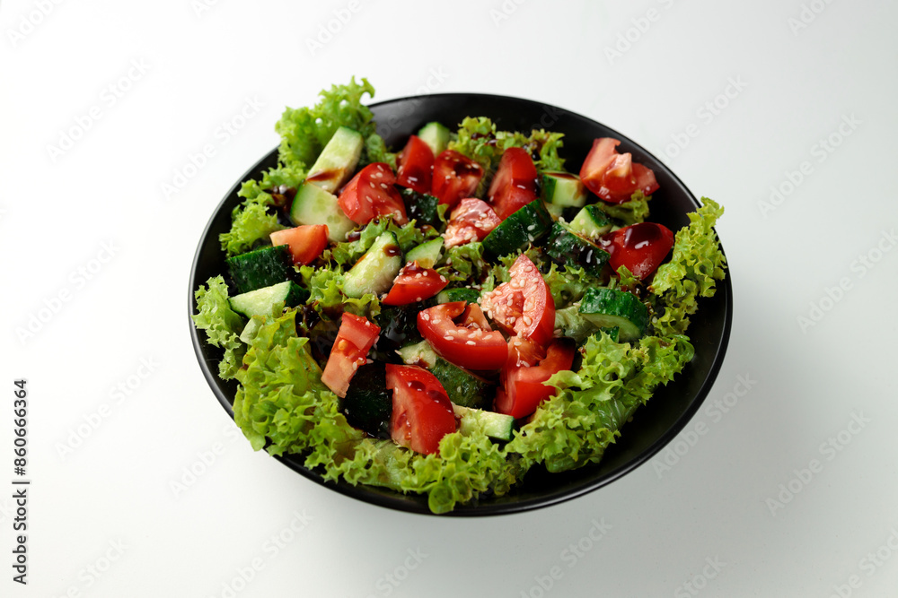 Vegetable salad of tomatoes, cucumbers, onions, lettuce dressed with aromatic dressing in a black plate on a white background Vegetable salad of tomatoes, cucumbers, onions, lettuce dressed with aromatic dressing in a black plate on a white background