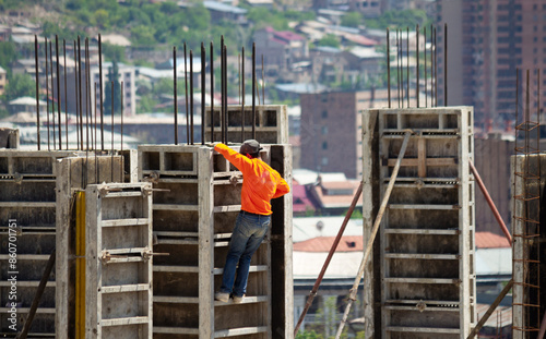 A construction worker climbs a formwork at a construction site on background cityscape.