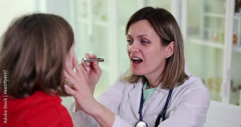 Focused doctor asks to open mouth wider to check throat of girl patient with shining flashlight. Professional medic in uniform does checkup in hospital slow motion Focused doctor asks to open mouth wider to check throat of girl patient with shining flashlight. Professional medic in uniform does checkup in hospital slow motion
