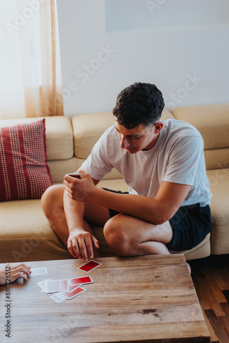 Young man engaged in a card game at home, seated around a wooden table in a cozy living room.