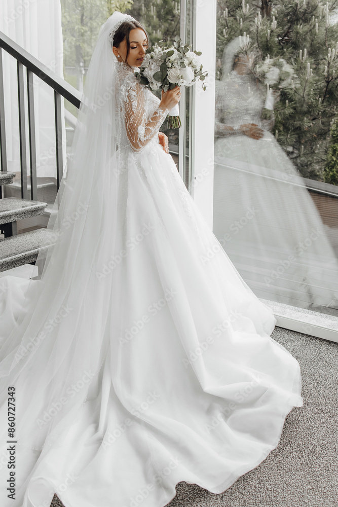 Obraz premium A bride is wearing a white wedding dress and holding a bouquet of flowers. The dress is long and flowing, and the bride is standing on a staircase. Concept of elegance and celebration