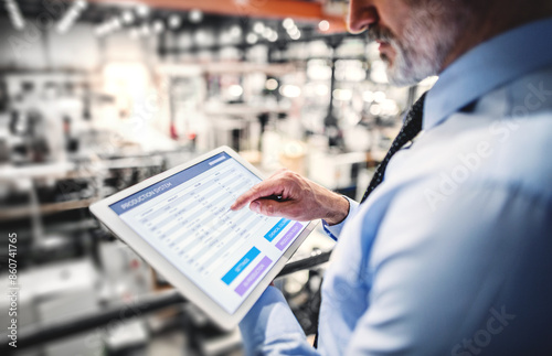 Portrait of project manager standing in modern industrial factory, holding tablet. Manufacturing facility with robotics, robotic arms and automation. Storing products and materials in warehouse. photo