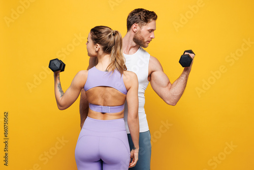 Fototapeta Naklejka Na Ścianę i Meble -  Back rear view young strong fitness trainer instructor sporty two man woman wearing blue clothes spend time in home gym hold dumbbells isolated on plain yellow background. Workout sport fit concept.