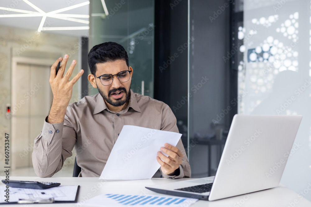 Young man looking stressed at paperwork in office setting Young man looking stressed at paperwork in office setting