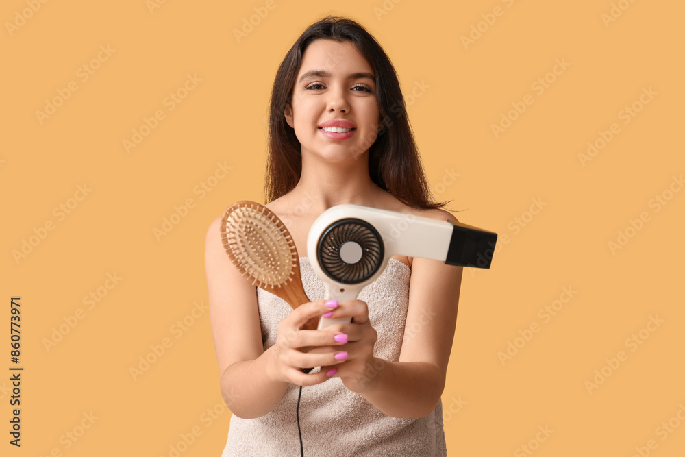 Obraz premium Beautiful young happy woman with towel, hair dryer and brush on yellow background