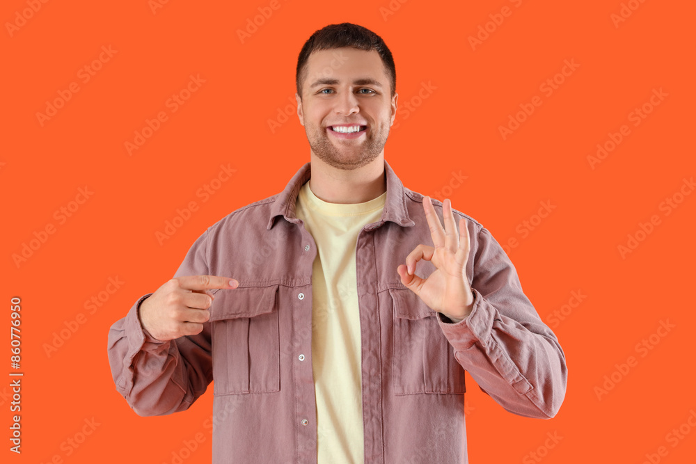 Handsome man pointing at OK gesture on orange background Handsome man pointing at OK gesture on orange background