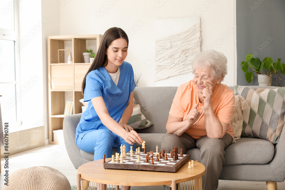 Obraz premium Young nurse with senior woman playing chess at home