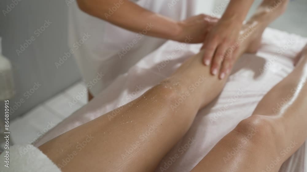 Cosmetology procedures. Applying scrub to a woman's legs in a beauty salon. Close-up of the hands of an unrecognizable female masseur wiping the legs of a woman lying on the table, slow motion. Cosmetology procedures. Applying scrub to a woman's legs in a beauty salon. Close-up of the hands of an unrecognizable female masseur wiping the legs of a woman lying on the table, slow motion.